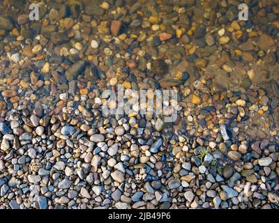 Kieselsteine an einem natürlichen Flussufer von oben. Blick von oben auf kleine Steine mit Schmutz und Wasser. Hintergrundtextur mit einem sanften Übergang. Stockfoto