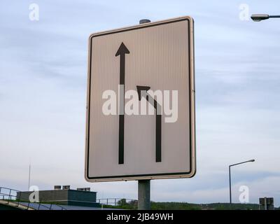 Fahren Sie in Deutschland auf das linke Verkehrsschild. Die rechte Spur endet und Autofahrer müssen in die linke Spur wechseln. Straßenschild mit Pfeilen. Stockfoto