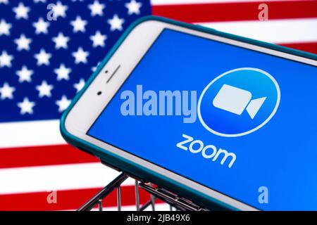 Logo der Zoom App, Videotelefonie- und Online-Chat-Dienste-App von Zoom Video Communications, Inc., auf dem iPhone im Warenkorb mit US-Flagge Stockfoto