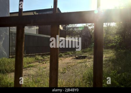 Verlassene Lagerhalle und ein Hof durch einen rostigen Zaun gesehen Stockfoto