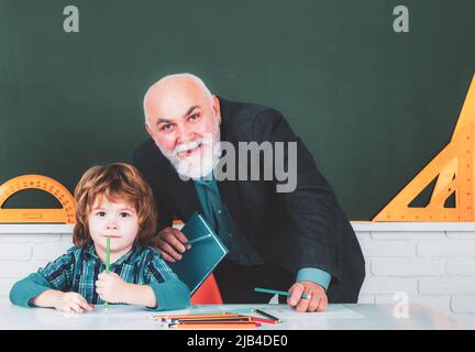 Großvater Lehrer mit Schüler auf der Rückseite des Klassenzimmers an der Grundschule. Individueller Unterricht. Porträt eines älteren Lehrers und eines kleinen Jungen Stockfoto