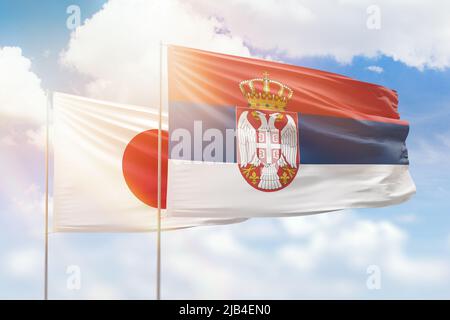 Sonniger blauer Himmel und Flaggen von serbien und japan Stockfoto