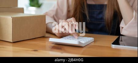 Asiatische Frau Unternehmerin mit Rechner mit Bleistift in der Hand, Berechnung der finanziellen Kosten zu Hause Büro, Online-Markt Verpackung Box Lieferung Stockfoto