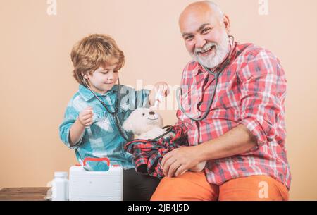 Kleiner Arzt. Charmanter kleiner Junge, der eine Wange seines Großvaters untersucht. Mann im bunten Strickschal mit Medizin. Älterer Mann mit kleinen niedlichen Stockfoto