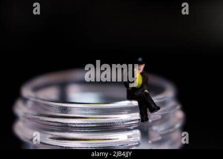 Miniatur-Geschäftsmann sitzt auf dem Hals der Plastikflasche. Der Mann im Bild telefoniert mit seinem Mobiltelefon. Stockfoto