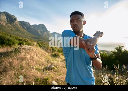 Schwarzer junger African American Erwachsener Mann konzentriert und Stretching vor seiner morgendlichen Übung auf dem schönen Berg. Draußen arbeiten Stockfoto