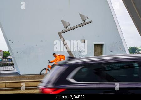 Ein Auto und ein Deliveryando-Fahrradkurier überqueren die Erasmus-Brücke bei windigem Wetter am 27,2022. Mai in Rotterdam, Niederlande. Stockfoto