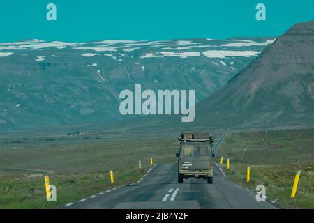 Rückansicht eines abenteuerlichen Offroad-Fahrzeugs, das durch isländische Straßen in Richtung Berge fährt. Epische Roadtrip mit einem Auto oder überfahrendem Fahrzeug. Stockfoto