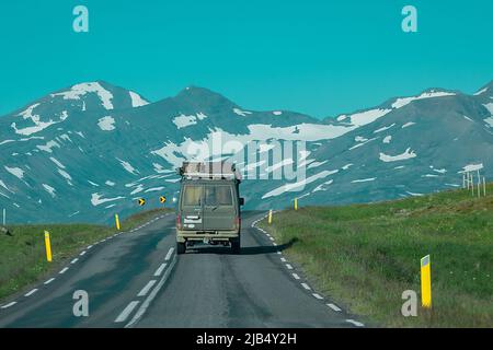 Rückansicht eines abenteuerlichen Offroad-Fahrzeugs, das durch isländische Straßen in Richtung Berge fährt. Epische Roadtrip mit einem Auto oder überfahrendem Fahrzeug. Stockfoto