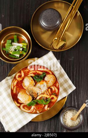 Jjampong koreanische Gewürznudelsuppe auf Golden Metal Bowl, serviert mit Green Onion Kimchi. Blick von oben auf dem Holztisch Stockfoto