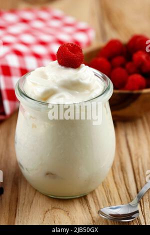 Ein Glas Joghurt mit wilden Himbeeren auf einem Holztisch Stockfoto