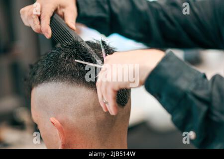 Crop unkenntlich Friseur Schneiden schwarze Haare von anonymen männlichen Kunden mit scharfen Scheren in modernen Friseursalon auf verschwommenem Hintergrund Stockfoto