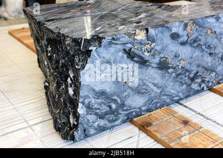 Hoher Winkel von großen Block aus schwarzem und Gold Portoro italienischen Marmor auf Holzbohlen auf Fliesenboden in der Werkstatt bereit geschnitten platziert werden Stockfoto