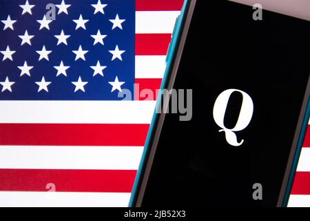 Kumamoto / JAPAN - Okt 20 2020 : das Logo von Qanon, einer rechtsextremen Verschwörungsgruppe, auf dem iPhone mit US-Flagge Hintergrund Stockfoto