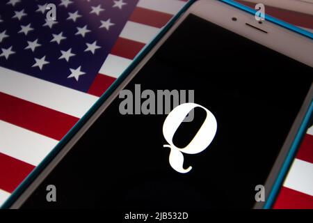 Kumamoto / JAPAN - Okt 20 2020 : das Logo von Qanon, einer rechtsextremen Verschwörungsgruppe, auf dem iPhone mit US-Flagge Hintergrund Stockfoto