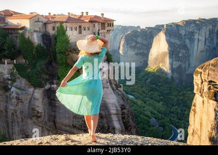 Junge Frau in grünem Kleid und einem Hut, die die Natur auf den Bergen in der Nähe von Meteora Klöstern genießt. Griechenland. Meteora - unglaubliche Sandsteinfelsen Stockfoto