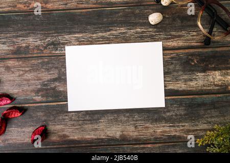 Feminines Desktop-Mockup mit leerer weißer Papierkarte, Vintage-Brillen, Ästen und Pot Pourri auf braunem Shabby-Tisch. Stilvolles Retro-Konzept Stockfoto