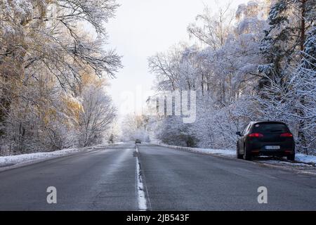 Das Auto steht am Straßenrand auf einer verschneiten Straße im Wald. Winterspur während des ersten Schnees. Stockfoto