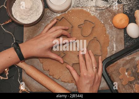 Kochen Weihnachten Lebkuchen Cookies auf einem dunklen Hintergrund. Lebkuchen mit einer Lebkuchenform aus dem Teig schneiden, Draufsicht, roher Teig mit Zimt Stockfoto