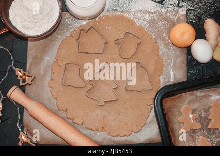 Kochen Weihnachten Lebkuchen Cookies auf einem dunklen Hintergrund. Lebkuchen mit einer Lebkuchenform aus dem Teig schneiden, Draufsicht, roher Teig mit Zimt Stockfoto