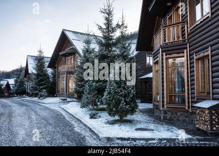 Schneebedeckte Häuser in den Bergen. Ferienhäuser in einem Skigebiet. Winterstraße. Ukrainische Winterkarpaten. Stockfoto