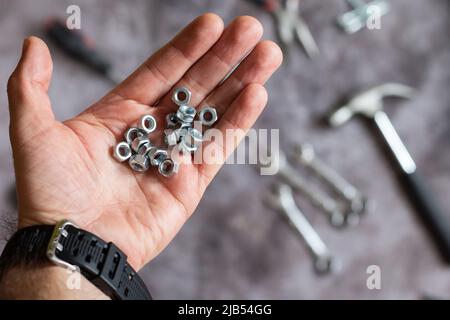 Viele Schraubenmuttern sind in der Hand. Hände mit Werkzeug. Satz von Werkzeugen für Hausreparatur. Hammer, Zange, Nägel, Nüsse. Stockfoto