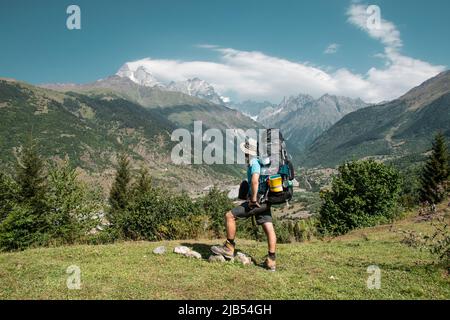 Wanderer Mann steht auf der Klippe gegen den Gipfel eines Berges. Der Mensch hat einen Rucksack und Wanderstöcke. Mountain Trekking. Platz kopieren Stockfoto