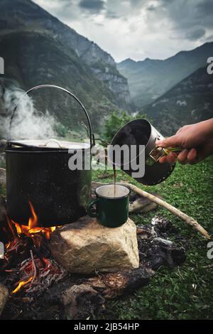 Auf einer Wanderung in die Kaukasusberge wird morgens Kaffee aus einer Kanne in eine Tasse gegossen Stockfoto