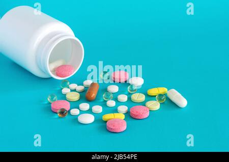 Viele Pillen werden aus einer Medikamentenflasche gegossen. Pillen und Pillen auf blauem Hintergrund. Medizinische Tabletten: Analgetika, Pyretika. Stockfoto