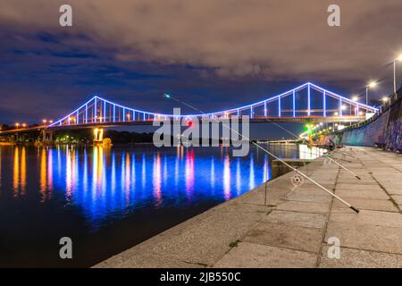 Nacht europäische Stadt in bunten Lichtern und Reflexion im Wasser, Kiew (Kiew) die Hauptstadt der Ukraine. Fußgängerbrücke über den Fluss Dnjepr und Vie Stockfoto
