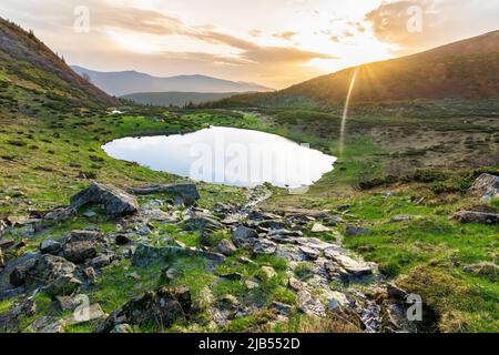 Morgendämmerung auf einem Bergsee in den Bergen, die ukrainischen Karpaten, den Woroscheska-See, die grünen Hänge, die Sonnenstrahlen, Ein blauer See hoch in den Bergen Stockfoto