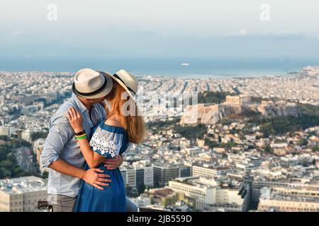 Ein paar verliebte Touristen küssen sich im Morgengrauen auf dem Berg Lycavitos in Athen. Das beste Panorama von Athen und der Akropolis. Im Hintergrund die Ägäis Stockfoto