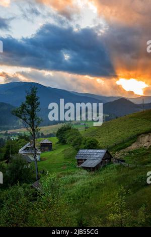 Sonnenuntergang in einem Bergdorf in den ukrainischen Karpaten. Grüne Berghänge und orange Strahlen der untergehenden Sonne., Ukraine, Europa. Stockfoto