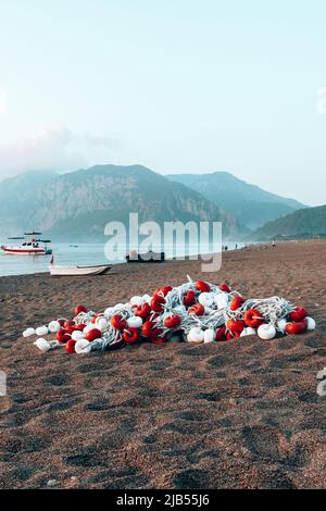 Am Morgen am Strand im Dorf Cirali liegen die Fischernetze auf dem gelben Sand. Boote und Schiffe in der Ferne des Taurusgebirges werden vertäut Stockfoto