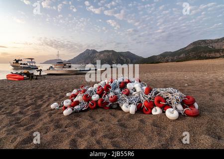 Am Morgen am Strand im Dorf Cirali liegen die Fischernetze auf dem gelben Sand. Boote und Schiffe in der Ferne des Taurusgebirges werden vertäut Stockfoto