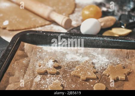 Kochen Weihnachten Lebkuchen Cookies auf einem dunklen Hintergrund. Lebkuchen mit einer Lebkuchenform aus dem Teig schneiden, Draufsicht, roher Teig mit Zimt Stockfoto