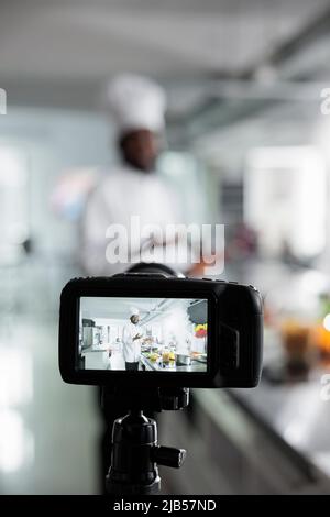 Nahaufnahme des Kameraaufnahmekopfkochs, der in der Restaurantküche ein Gourmet-Gericht für die Kochschule zubereitet. Meisterkoch kocht Abendessen während Dreharbeiten Kreation für Gastronomie Schule. Stockfoto