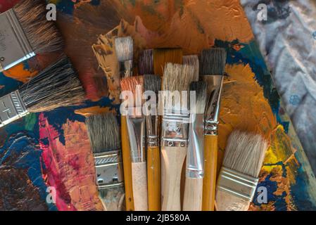 Pinselsammlung auf der alten Palette Draufsicht. Mischen verschiedener Ölfarben im Kunststudio Stockfoto