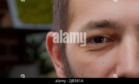 Makroaufnahme eines männlichen Models, das ein Auge auf der Kamera zeigt, braune Augen hat und lächelt. Junger Mann mit authentischem Aussehen und gesunder Sicht, mit positiven Gesichtsausdrücken. Nahaufnahme. Stockfoto