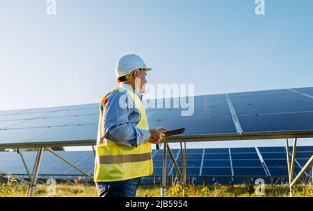 Arbeiter überprüft Solarzellen mit Tablet in Solarfarm. Ökoenergie Stockfoto