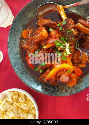 Geschmorte Schweinefleischrippen mit Gemüse in einer würzigen Sauce auf einem Teller auf einem Tisch mit einer roten Tischdecke. Asiatische Küche. Draufsicht Stockfoto