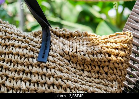 Trendiger Rattan Strohsack und tropisches Palmenblatt auf dem Hintergrund. Tropische Palmenblätter. Nahaufnahme einer Strohsommer-Rattan-Tasche. Sommerurlaub Stockfoto