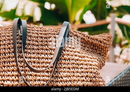 Trendiger Rattan Strohsack und tropisches Palmenblatt auf dem Hintergrund. Tropische Palmenblätter. Nahaufnahme einer Strohsommer-Rattan-Tasche. Sommerurlaub Stockfoto