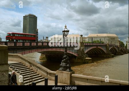 LondonUK - 29. Mai 2022: Blick über die braune / farbige Themse und Lambeth Brücke mit vorbeifahrendem roten Bus und millbank Turm an sonnigen Tag mit Stockfoto