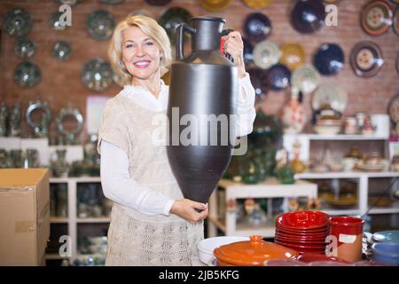 Lächelnde reife Frau mit Keramikgeschirr Stockfoto