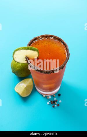 Hausgemachter Michelada-Cocktail mit Bier, Limettensaft, heißer Sauce, gesalzenem Rand und Tomatensaft auf blauem Hintergrund Stockfoto