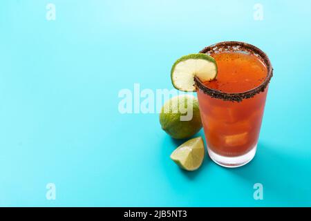 Hausgemachter Michelada-Cocktail mit Bier, Limettensaft, heißer Sauce, gesalzenem Rand und Tomatensaft auf blauem Hintergrund Stockfoto