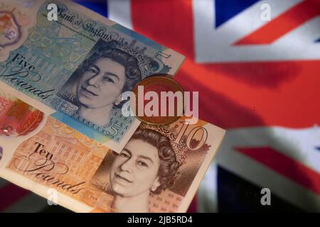 Zwei britische fünf- und zehn-Pfund-Scheine und eine-Pfund-Münze auf der Flagge des Vereinigten Königreichs. Stockfoto