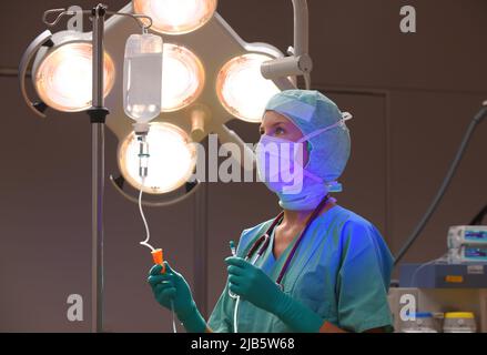 In einem Operationssaal wird eine Krankenschwester aus dem Betanestheater gesehen. Sie wird in grüner steriler medizinischer Kleidung mit einer Gesichtsmaske über ihrem Gesicht gesehen. Stockfoto