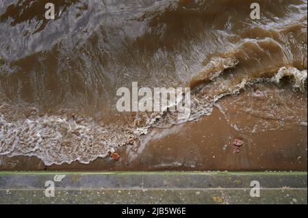 Blick hinunter auf Wellen, die über Sand in braunem Wasser brechen Stockfoto